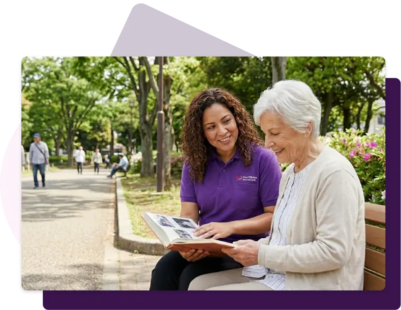 A HeartMates caregiver and an older woman looking through a photo album together on a park bench.